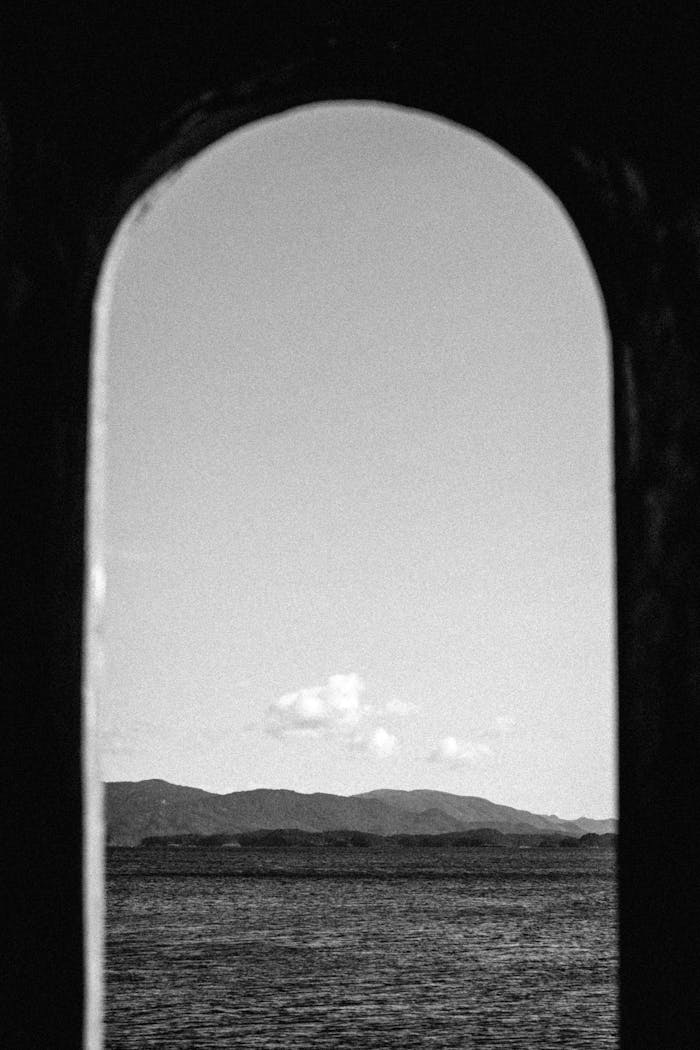 Black and white photo of the sea and mountains framed by an arched window.