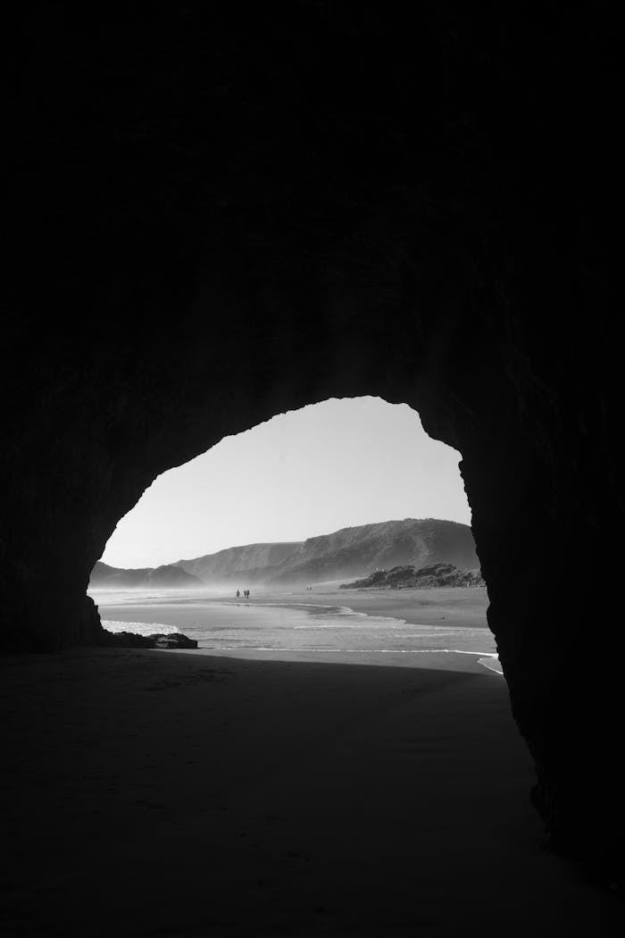 Explore the stunning coastline through a dramatic cave entrance, captured in timeless black and white.
